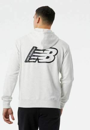 Sudadera gris claro con una capucha amplia, textura suave y puños acanalados. Presenta un gran logo negro de "New Balance" en la parte de atrás.