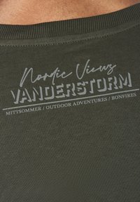 Olive green fabric t-shirt with ribbed texture, featuring white printed text: "Nordic Views VANDERSTORM" and "MITTSOMMER / OUTDOOR ADVENTURES / BONFIRES."