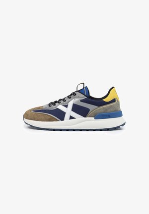 Męskie sneakersy z połączeniem szarego zamszu i granatowej tkaniny, niebieskimi akcentami, białym logo i grubą białą podeszwą z niebieską podeszwą zewnętrzną.