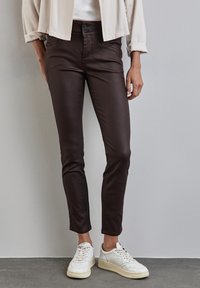 Bruna slim-fit byxor med en slät textur, med dubbelknäppning och framlommor, ihop med vita sneakers.