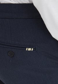 Pantaloni blu navy con un tessuto testurizzato, dotati di chiusura frontale con bottone e una piccola tasca accentuata con una striscia color crema.