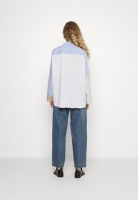 Randig skjorta med knappar och paneler i blandade tyger i blått, grönt och vitt. Avslappnad passform, långa ärmar och detaljer med veck bak. Denimbyxor och svarta skor.