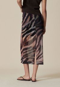 Gonna trasparente di media lunghezza con motivo a strisce nere e marroni. Presenta spacchi laterali e una texture leggera e fluente.