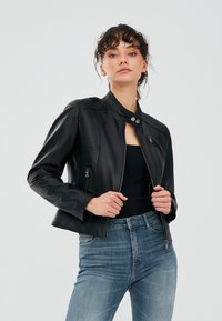 Zwarte leren jas met een opstaande kraag, ritssluiting aan de voorkant en twee zijzakken. Heeft fitted mouwen en subtiele stikdetails.