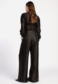 Schwarze Spitze Langarmoberteil mit Zickzackmuster, kombiniert mit hoch taillierten schwarzen weit geschnittenen Hosen mit Taschen und glatter Textur.