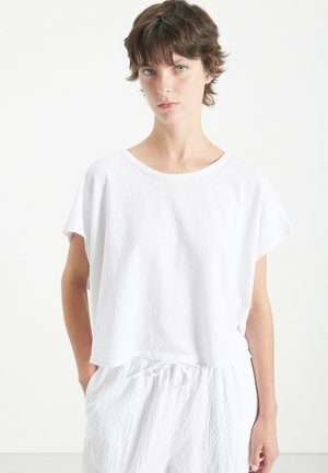 Hvid kortærmet T-shirt i blød kvalitet med løs pasform og bred halsudskæring, parret med hvid tekstureret bukser med snoretræk.