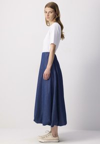 Haut blanc à manches courtes avec une jupe en jean bleu marine, dotée d'un design évasé. Le modèle porte des baskets beiges.