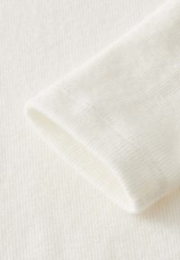 Weißer Baumwollstoff mit gerippter Textur, der eine umgeschlagene Kante aufweist. Das Material wirkt weich und glatt und präsentiert ein klares, einfaches Design.