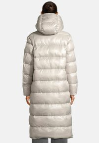 Lichtgrijze lange donzen jas met horizontale stiksels, oversized capuchon en glanzende textuur, met een knielange snit en een relaxte pasvorm.