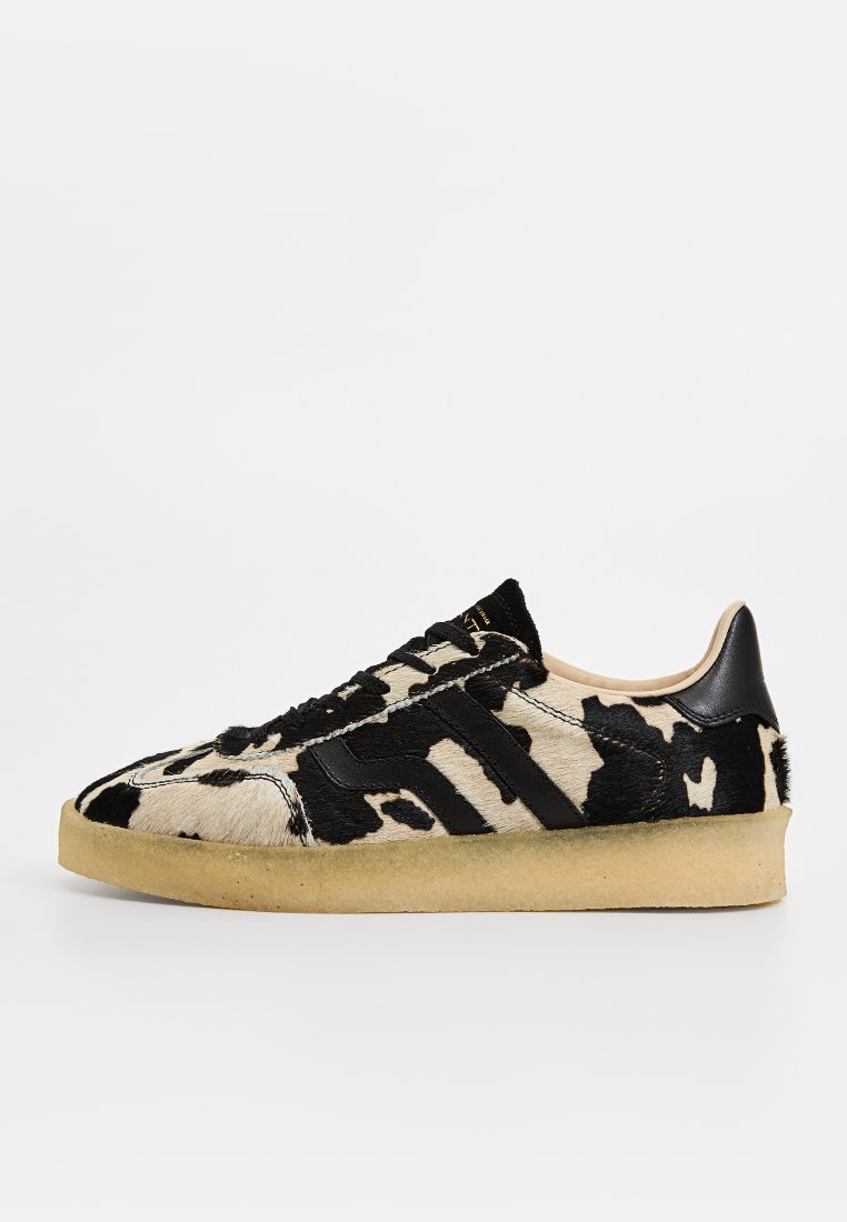 Schwarz-weiße Sneaker mit Kuhmuster, einer strukturierten Oberseite, schwarzen Akzenten und einer beigen Gummisohle. Schnürdesign und runde Zehen.