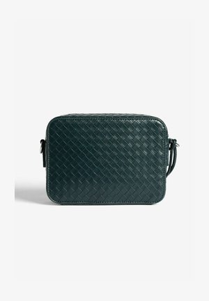 Woven leather crossbody bag in dark green. Rectangular shape with rounded corners and a textured surface. Adjustable strap on side.