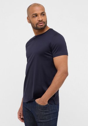 Navy blue short-sleeve t-shirt with a round neckline. Made of smooth fabric. The fit is relaxed, paired with dark blue jeans.