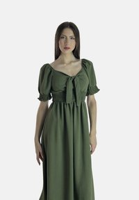 Robe longue verte olive avec une taille cintrée, détail à nœud au col, et manchons froncés. Tissu doux et texturé.