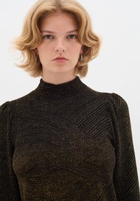 Top nero a maniche lunghe con collo alto, caratterizzato da un motivo a spirale dorato testurizzato e maniche leggermente a sbuffo. Tessuto liscio, design aderente.