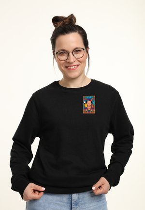 Sweat-shirt noir en tissu doux avec un patch imprimé coloré sur la poitrine, représentant un portrait stylisé avec des accents floraux.