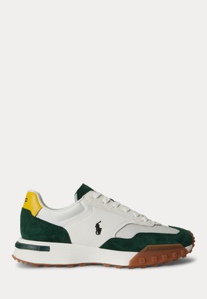 Sneaker bianca e verde scuro con linguetta del tallone gialla, logo nero, lacci bianchi e suola marrone texturizzata su uno sfondo chiaro.