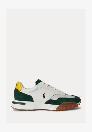 Sneaker bianca e verde scuro con linguetta del tallone gialla, logo nero, lacci bianchi e suola marrone texturizzata su uno sfondo chiaro.