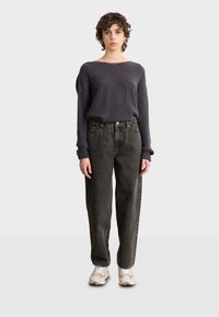 Dunkelgrauer, strukturierter Pullover mit Rippstrick, kombiniert mit lockeren, geraden schwarzen Jeans und beige Sneakern. Einfaches, lässiges Outfit.