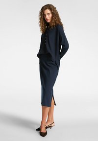 Marinblå stickad topp med lång ärm och knapprad, tillsammans med en knälång kjol med sidslitsar och en figursydd silhuett.