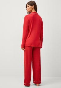 Rode pyjama-set van zachte stof; lange mouwen top met witte bies op de kraag en manchetten, gecombineerd met bijpassende loszittende broek.