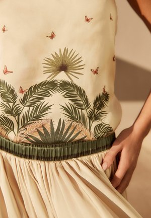 Beżowy top bez rękawów z zielonymi i różowymi nadrukami botanicznymi, z motywami palm i motyli. Zebrana oliwkowo-zielona talia.