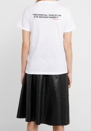 Person wearing white t-shirt with quote "The essential thing in life is to reinvent oneself" and black leather skirt, viewed from behind.