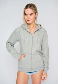 Felpa con zip grigia chiara, con tasca anteriore, cappuccio con cordino e polsini a coste. Tessuto morbido e vestibilità comoda. Abbinate a shorts di denim.