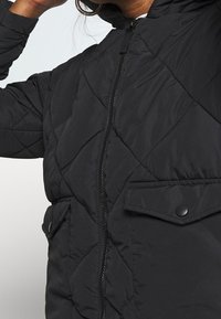 Černá prošívaná bunda s předním zipem, kapsami na patentky a strukturovanou tkaninou s diamantovými vzory. Kapucňový design.