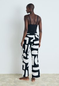 Črna brezrokavnik kombiniran z širokimi hlačami z drzno črno-belo geometrijsko obliko, izdelanimi iz lahkega materiala, sproščenega kroja.