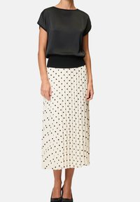 Czarna bluzka z krótkim rękawem i dzianinowym paskiem w talii, zestawiona z plisowaną, kremową spódnicą w czarne kropki. Dopełniona czarnymi butami.