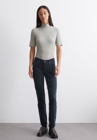 Lichtgrijze korte mouwen coltrui gecombineerd met donkerblauwe rechte jeans. Model draagt zwarte loafers. Gladde stof met een aansluitend ontwerp.