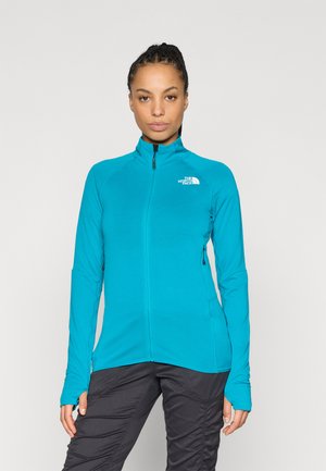 Žalsvai mėlyna striukė su užtrauktuku, aukštu apykakliu ir ilgomis rankovėmis, turinti tekstūruotą dizainą ir logotipą kairėje krūtinės pusėje.