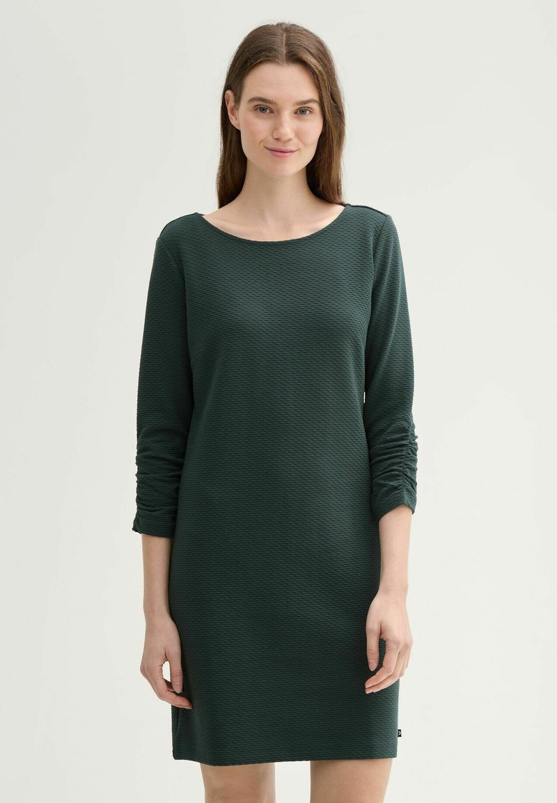 Texturált sötétzöld ruha kerek nyakkivágással és hosszú ujjakkal, ráncolt részletekkel az ujjakon és egyenes szabással.