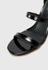 Sandale en cuir verni noir avec deux bandes larges sur le dessus, un semelle confortable lisse et un petit talon arrondi.