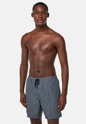 Costume da bagno grigio con un design testurizzato, vita elastica e cordino nero. La vestibilità è rilassata, raggiungendo la metà della coscia.