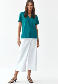 T-shirt verde acqua a scollo a V con maniche corte, abbinato a pantaloni bianchi a gamba larga e sandali neri con cinturini. Tessuto morbido e vestibilità rilassata.