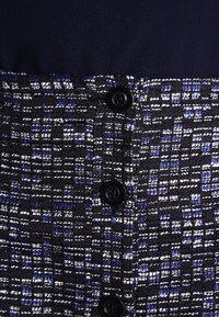 Tessuto a motivi blu e neri con texture intrecciata, con accenti bianchi e tre bottoni neri al centro.