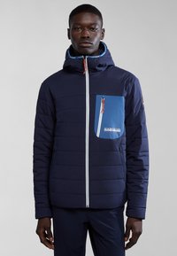 Giacca a vento navy con tasca sul petto blu, zip bianca e tirazip arancione. Presenta un cappuccio e una texture trapuntata su tutta la superficie.