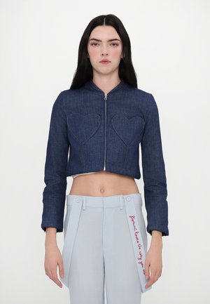 Beskuren blå jeansjacka med hjärtformade fickor, hög krage och frontdragkedja, kombinerad med ljusblå skräddarsydda byxor.