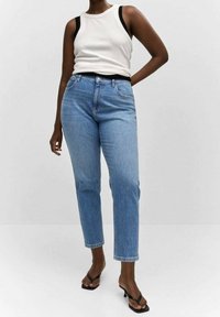 Vaqueros de mezclilla azul claro con corte recto, cintura alta, cinco bolsillos y costuras mínimas. Combinados con una camiseta sin mangas crema.