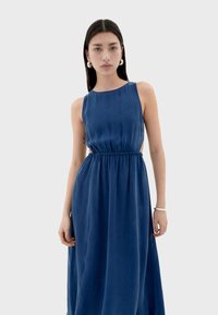 Vestido maxi de tela azul profundo, con cintura ajustada, diseño sin mangas y cortes laterales. Textura suave, caída elegante.