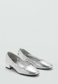 Ballerine metallizzate argento con finitura texturizzata, dotate di un tacco basso e design a punta arrotondata. La fodera interna è liscia.