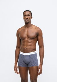 Marineblå boxershorts med mønster og en hvid elastisk linning med "TOMMY HILFIGER"-logo. Midi-længde med tætsiddende pasform.