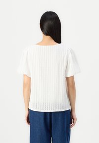 Hvit teksturert bluse med pufferm, med vertikale striper og rund hals, kombinert med løst sittende blå denimbukser.