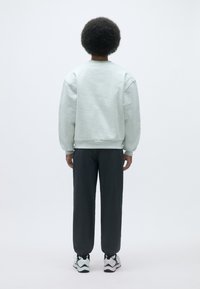 Sudaderas gris claro con hombros caídos, combinadas con pantalones oscuros ajustados gris, y zapatillas en blanco y negro. Simple, ajuste relajado.