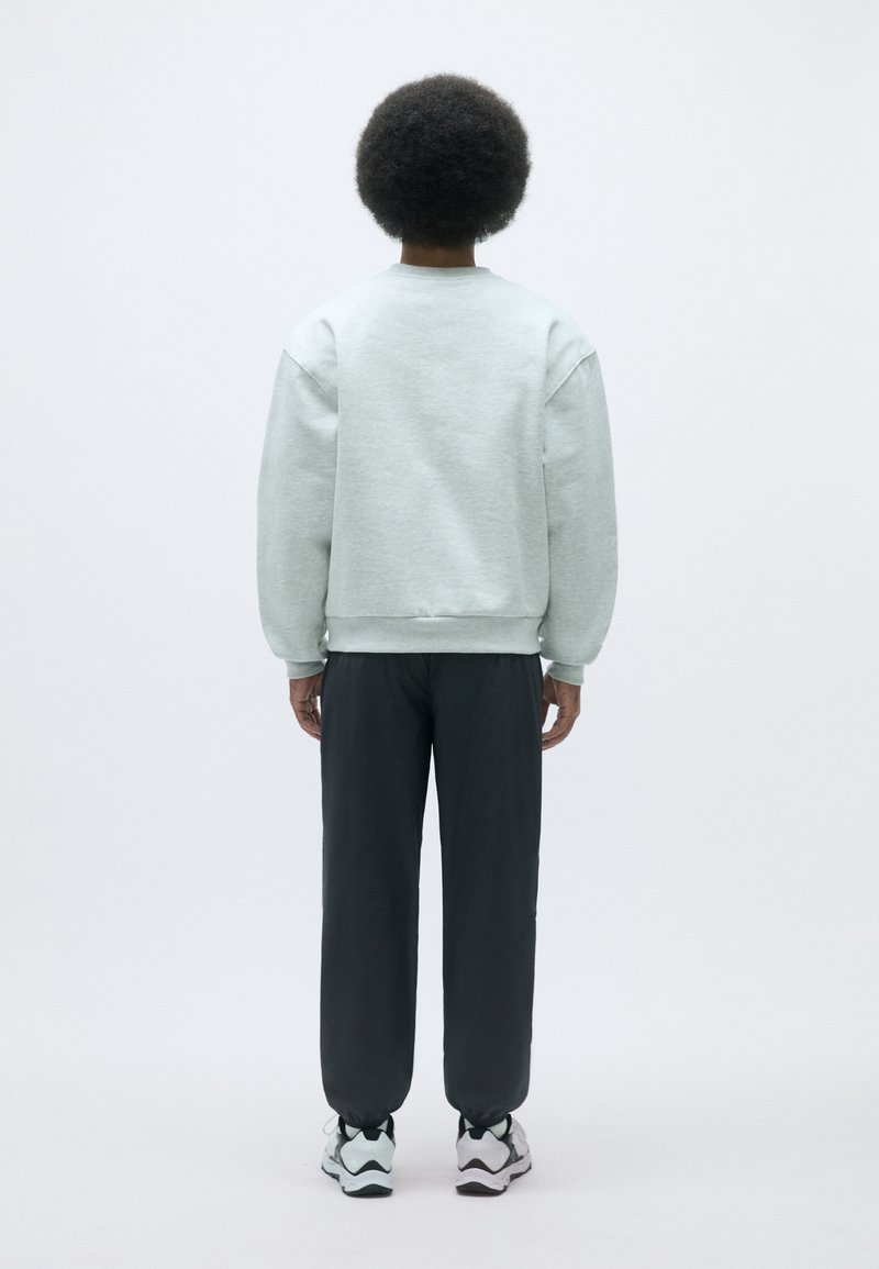 Helle graue Sweatshirts mit überschnittenen Schultern, kombiniert mit dunkelgrauen, schmal zulaufenden Hosen und schwarz-weißen Turnschuhen. Schlichte, lockere Passform.