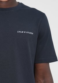 Tengerészet kék pamut póló, klasszikus környakú és rövid ujjú, fehér hímzett "LYLE & SCOTT" logóval a bal mellen.