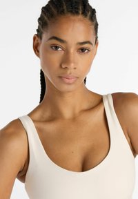 Top beige ajustado sin mangas con escote redondo, textura suave y tirantes anchos, mostrando un diseño limpio y minimalista.