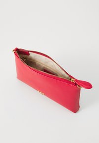 Sacca rossa in pelle con zip dorate, texture liscia e rivestimento interno beige. Design compatto per piccoli oggetti.