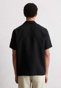 Schwarzes kurzärmliges Hemd aus leichtem Stoff mit Kragen und entspanntem Schnitt, mit einer einfarbigen Textur und einem geraden Saum am unteren Ende.